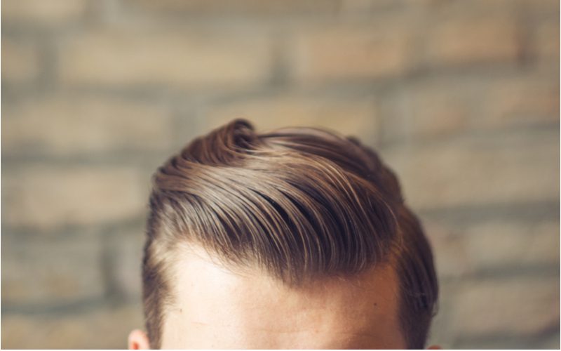 Kaukasische man met hipster kapsel op een man met slicked back haar staande voor een bakstenen muur