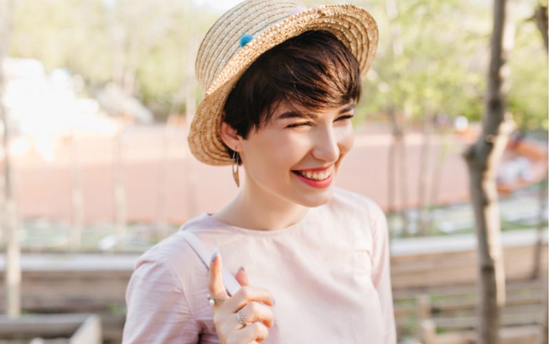 Een hack voor stap 4 in hoe een pixie cut te laten groeien toont een vrouw die een hoed draagt en glimlacht terwijl haar haar groeit.