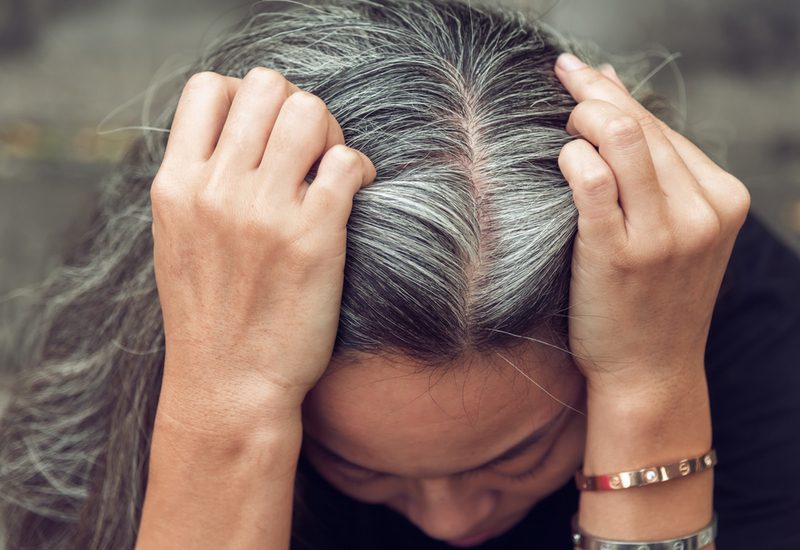 Vrouw houdt haar hoofd vast nadat ze ons heeft laten zien hoe je kleurgevende conditioner op haar grijze haar aanbrengt.