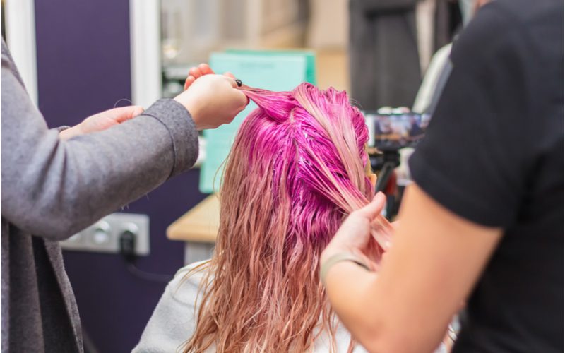 Afbeelding voor een stuk over wat permanente haarverf van de huid verwijdert met een vrouw in een salonstoel die roze haar krijgt