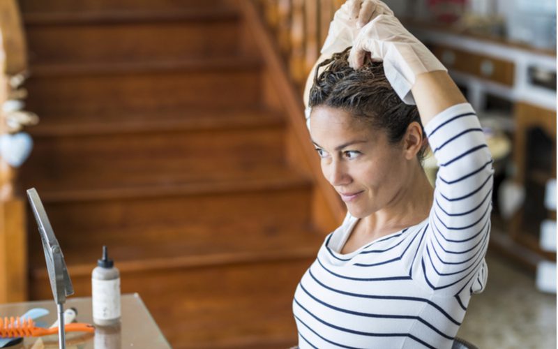 Vrouw die thuis haar haar verft terwijl ze in een spiegel kijkt