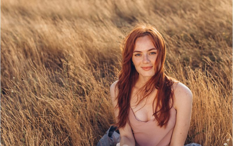 Dame die een lichtroze hemdje draagt met een ton aan decolleté blootgesteld terwijl ze ook auburn haar rockt terwijl ze in een tarweveld zit.