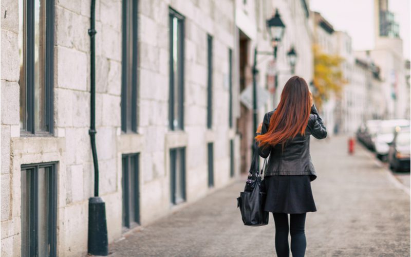 Foto achter een vrouw die over de stoep loopt en haar kastanjebruine haar in de wind laat wapperen.