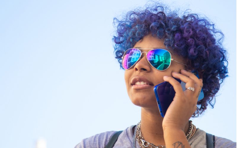Violetblauw, een favoriete haarkleur voor de bruine huid, op een vrouw die praat op een smartphone met een blauw hoesje.