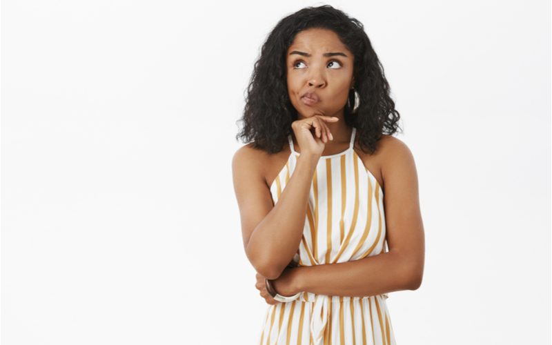 Afro-Amerikaanse vrouw in een gouden en witte jurk die haar armen kruist en haar kin vasthoudt en zich afvraagt wat de beste haarkleur is voor een bruine huid.