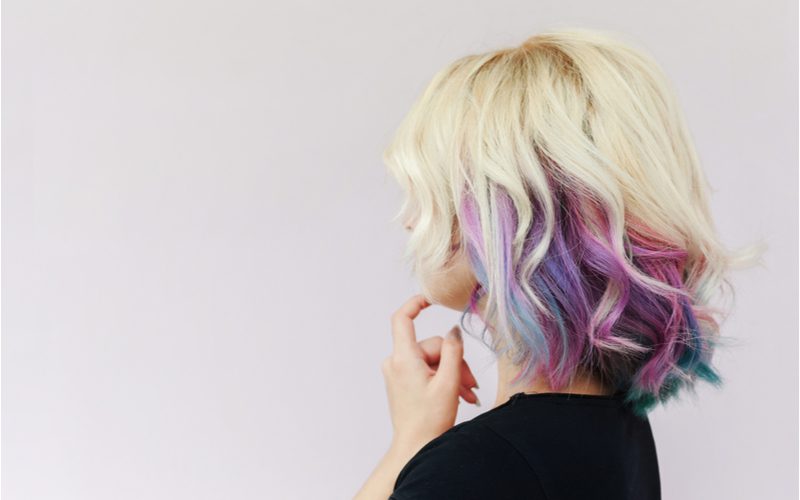 Vrouw met blond en paars tweekleurig haar in een zwart shirt die haar kin vasthoudt met haar linker wijsvinger