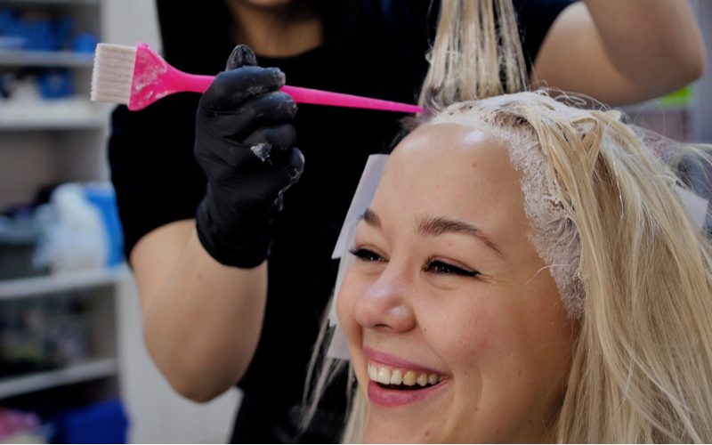 Afbeelding om te helpen beantwoorden hoe vaak kun je je haar bleken met een Aziatische vrouw in een salonstoel die haar haar laat verven met een bleekborstel met een rattenstaartuiteinde