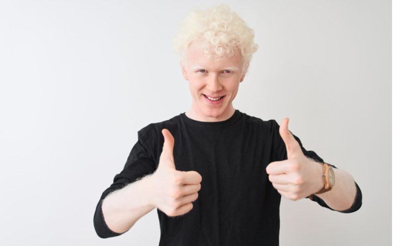 Bleke man met gebleekt blond haar draagt een zwart shirt en geeft een duim omhoog