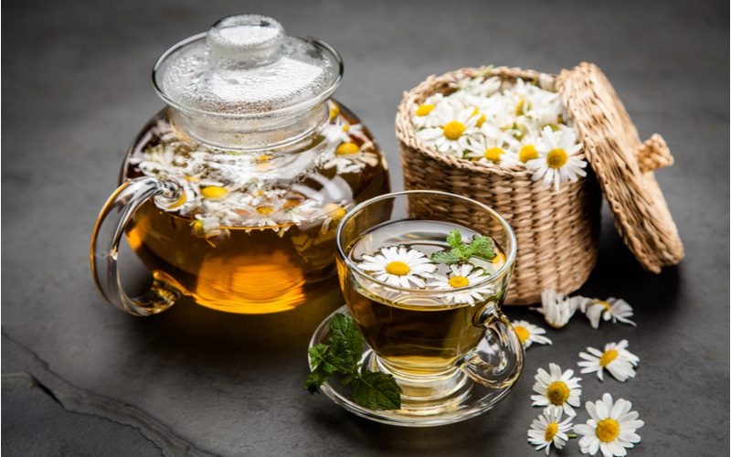 Foto van kamillethee zittend op een tafel naast een grote mand met bloemen om het haar lichter te maken zonder bleekmiddel