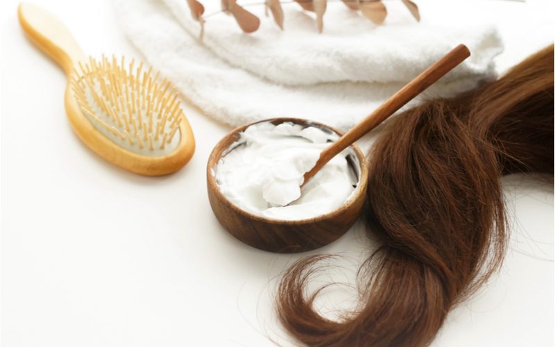Voor een stuk over hoe het haar op te lichten zonder bleekmiddel, staan een aantal haarproducten op een toonbank naast een lange streng bruin haar.