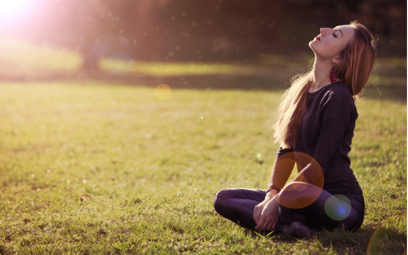 Mooie jonge vrouw zittend in de zon op een grasveld