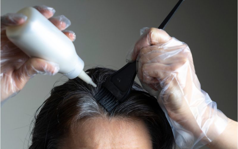 Voor een stuk over hoe lang het duurt om je haar thuis te verven, giet een vrouw een DIY haarverfkit op een borstel op haar haar