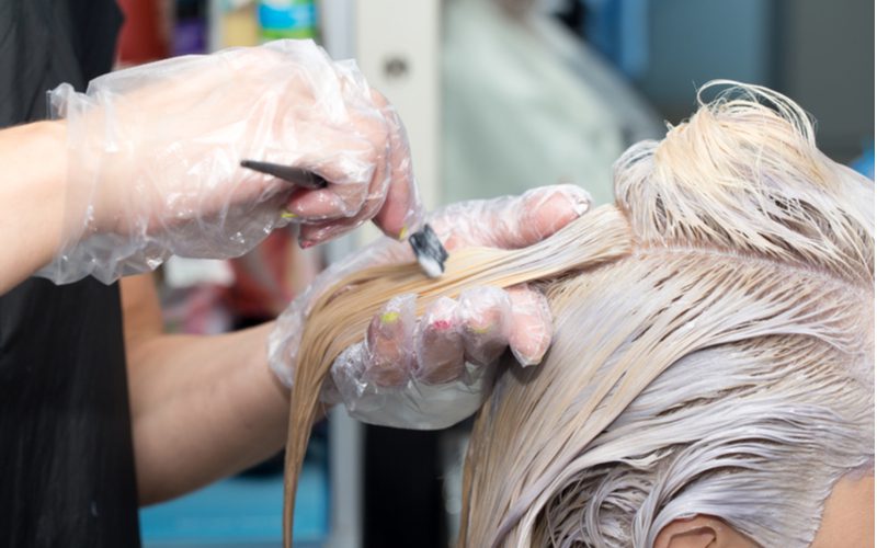 Om te illustreren hoe lang je bleekmiddel in het haar moet laten zitten, verft een vrouw met handschoenen het haar van een vrouw in een salon