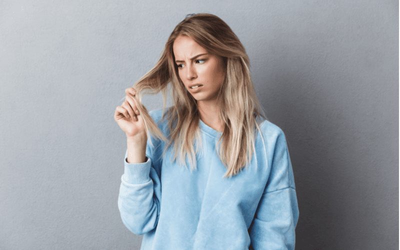 Voor een stuk over hoe haar te bleken, inspecteert een vrouw haar punten om uit te zoeken of het bleekmiddel het zal beschadigen.