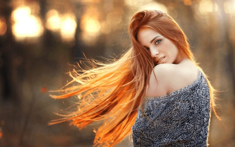 Dame met lang rood haar houdt haar afval en draagt een trui over haar schouder in de herfst