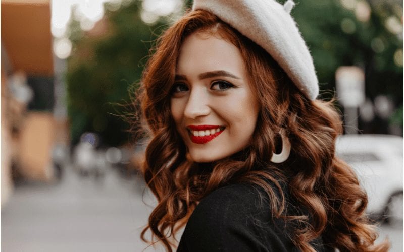 Franse vrouw die zich omdraait op een straat met gepolijste auburn krullen en rood haar