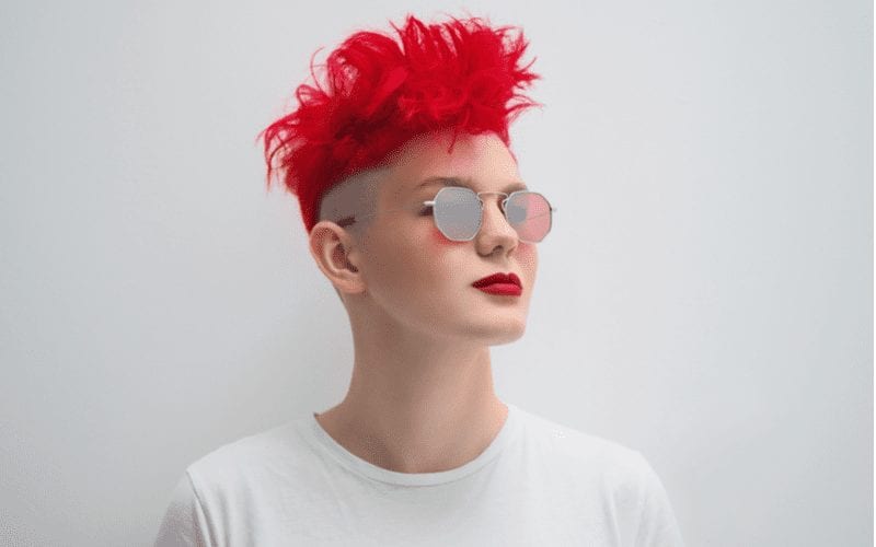Foto van een vrouw met een rood stekelig kapsel die een zonnebril draagt en omhoog kijkt