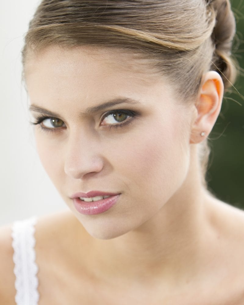 Vrouw met een teruggetrokken kapsel in een wit kanten hemdje kijkt vanuit haar ooghoek naar de camera.