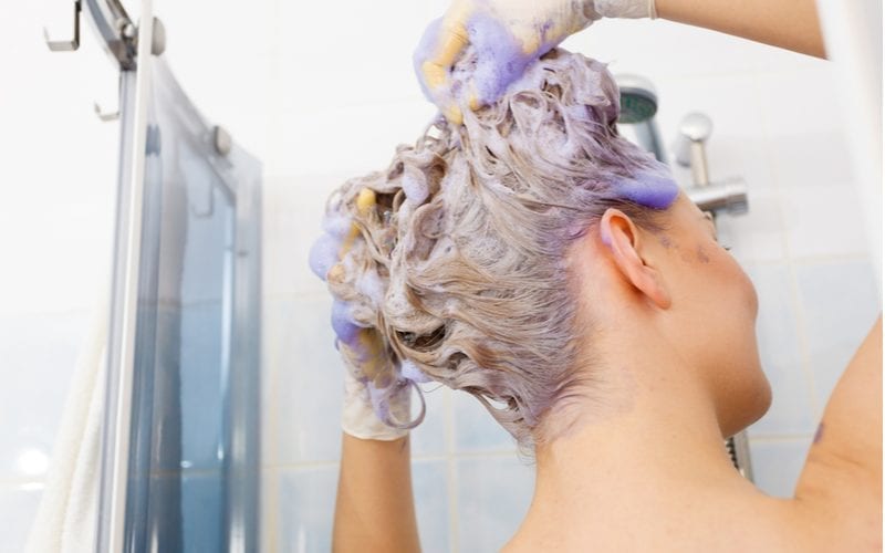Vrouw wast haar toner uit haar haar in een douche met paarse shampoo erin