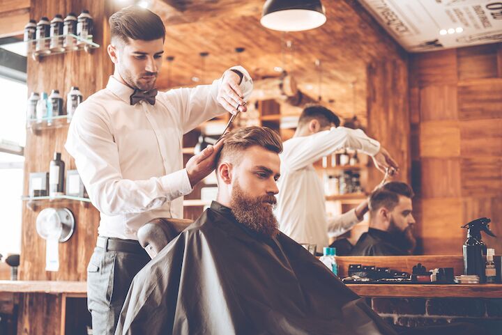 Kapper die het haar trimt van een man met een baard