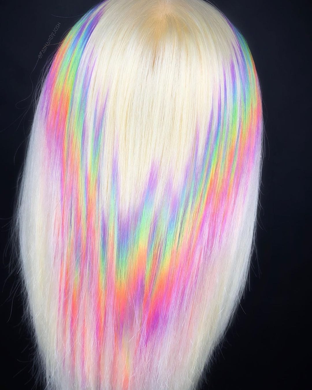 Gekarteld regenboog holografisch haar op een blonde vrouw die in een studio staat met uitzicht op de zwarte muur.
