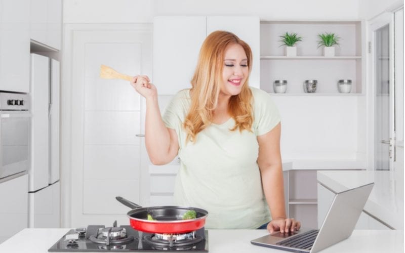 Beeld van een gelukkige vrouw die groenten op een rode pan in de keuken kookt