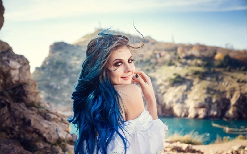 Vrouw staat met blauw haar en kijkt terug naar de camera voor meren en kliffen