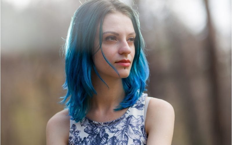 Jonge vrouw met donker haar dat overgaat in blauwe wortels draagt een lipstick