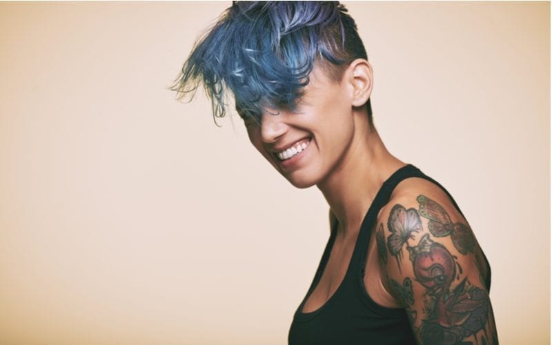 Vrouw met blauw haar en een zwarte tanktop met een tattoo op haar bovenarm