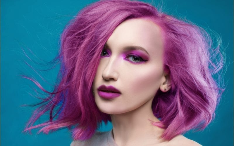 Vrouw met fel paars haar in verschillende tinten laat het wapperen in de wind terwijl ze paarse lippenstift draagt.