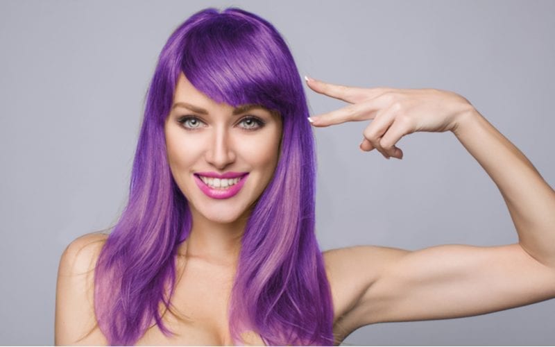 Aantrekkelijke rondborstige vrouw houdt een zijwaarts vredesteken omhoog naar haar paarse haar