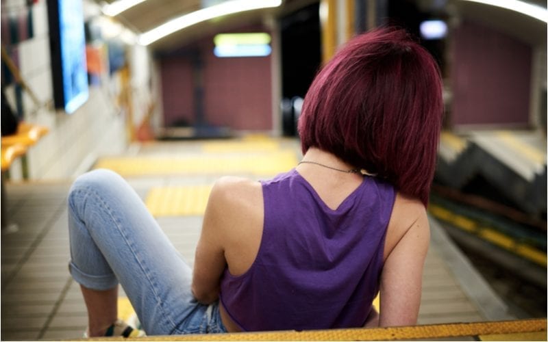 Vrouw in een paars shirt kijkt weg van de camera en zit op een metroperron