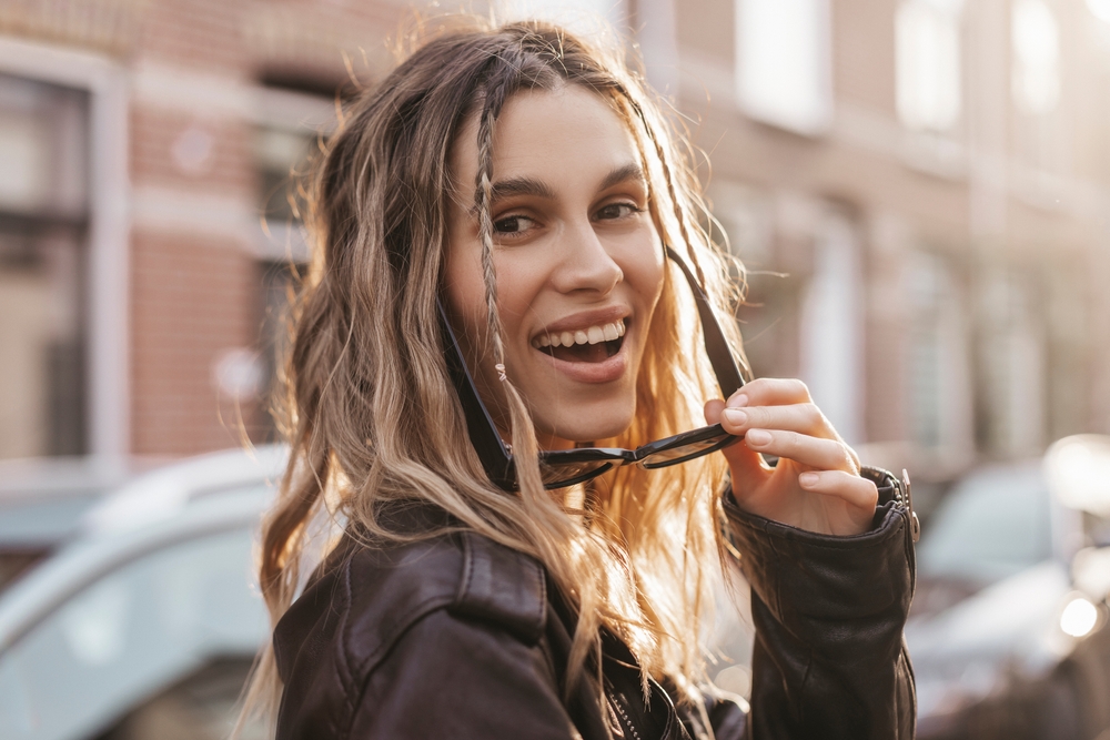 Baby Braids, een throwback y2k kapsel, afgebeeld op een peinzende vrouw in een leren jas.