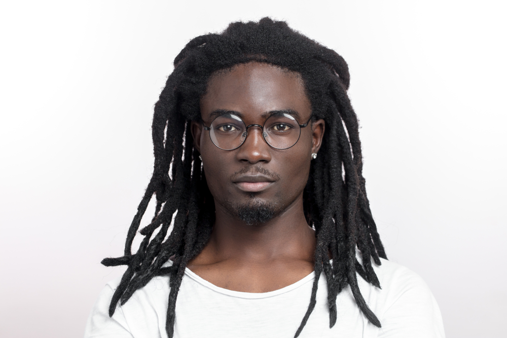 Wick Dreads kapsel op een man met een bril in een witte kamer