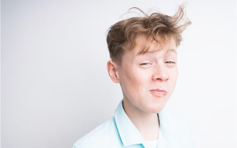 Voor een stuk over messy hair jongensstijlen, draagt een jongen met messy hair een floppy kapsel op zijn hoofd en een wit button-up shirt