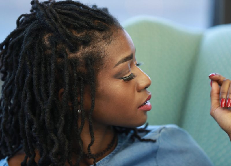 Vrouw die een blauw jeans shirt draagt met Half-Up Sisterlocks kijkt naar links.