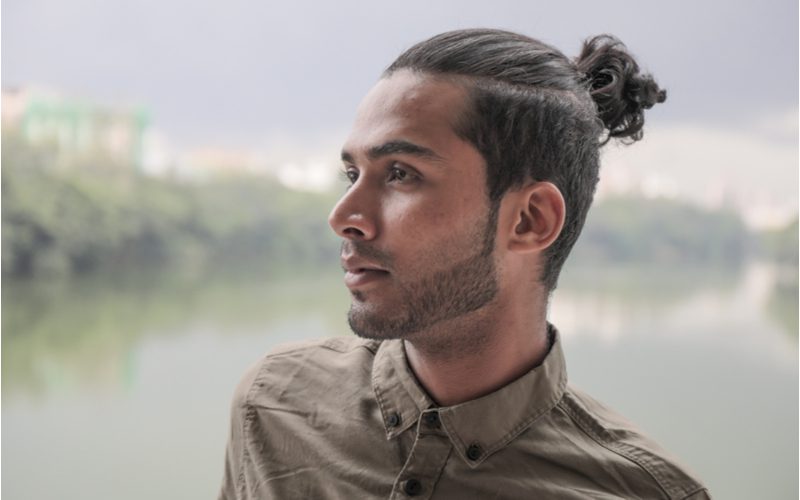 Half Up With Shaved Sides man bun op een licht aziatisch uitziende man die voor een rivier staat.