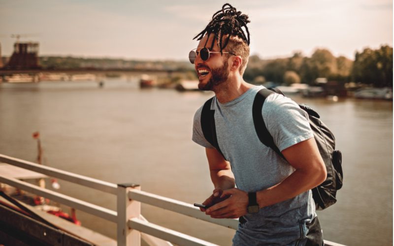 Gevlochten Top Knot Man Bun Kapsel gedragen door een man in een rugzak staand voor een rivier