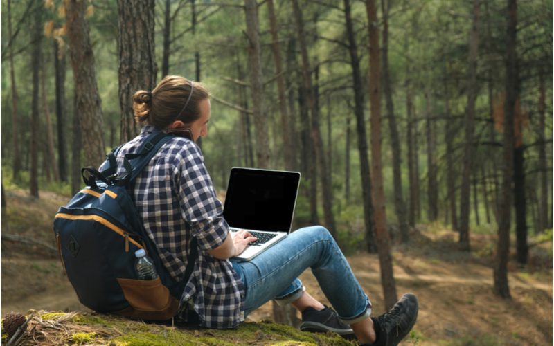 Man in een geruit overhemd buiten zittend werkend op een laptop met een Mid Looped Man Bun Met Hoofdband