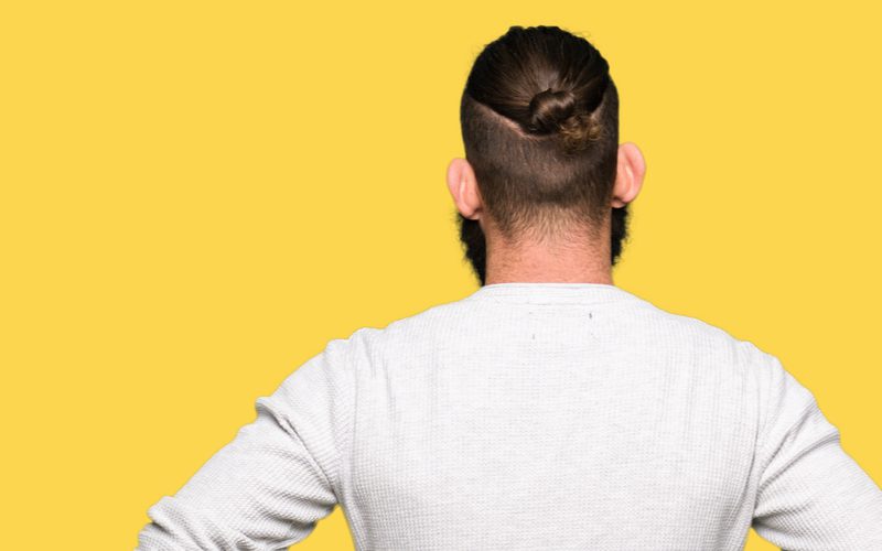 High Drop Undercut With Loop Man Bun op een man die een wit henley shirt met lange mouwen draagt.