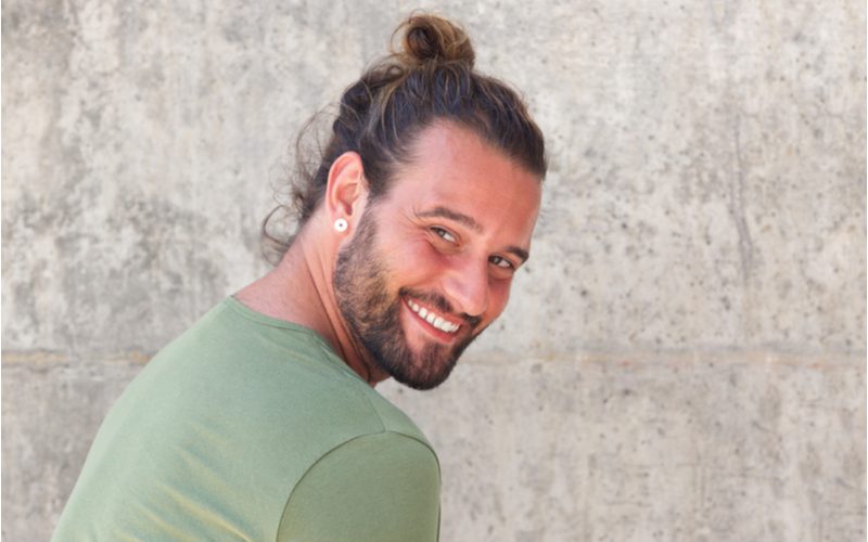 Messy and Casual Looped Man Bun op een man die over zijn schouder lacht in een grijze kamer.