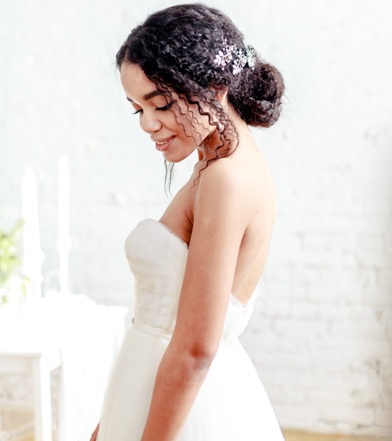 Afro-Amerikaanse bruid die een natuurlijke chignon met losse stukken en een bloemenaccent draagt.