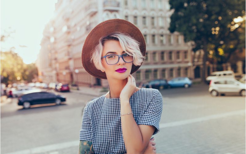 Side-Swept Bangs op een vrouw in een blauw en wit geruit shirt met een boho-stijl hoed.