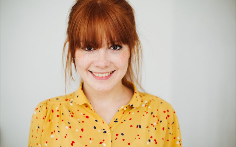 Wispy Full Fringe soorten pony's op een meid in een geel gespikkeld shirt met sproeten en rood haar.