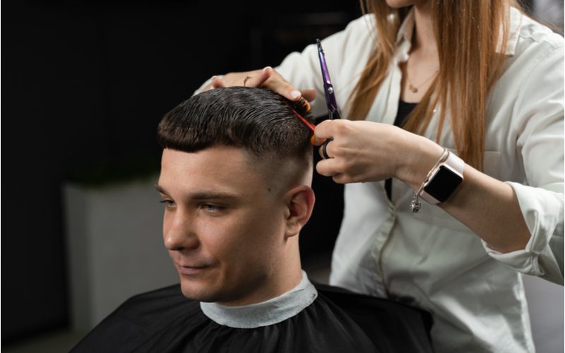 Caesar Crop kapsel voor een terugwijkende haarlijn wordt geknipt door een vrouw in een witte jas en een schaar