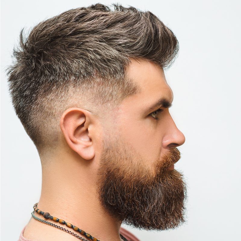 Man met een Faux Hawk Bald Fade, een van de beste kapsels voor terugwijkende haarlijnen, op een man in een zalmkleurig overhemd.