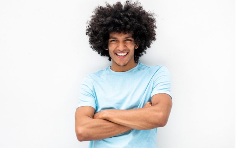 Defined and Tapered Fro, een zwart mannenkapsel, op een man die zijn armen kruist in een blauw shirt