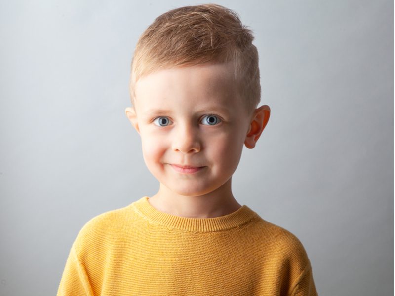 Side-Swept Crew Cut op een kleine jongen in een oranje trui voor een stuk over kleine jongenskapsels