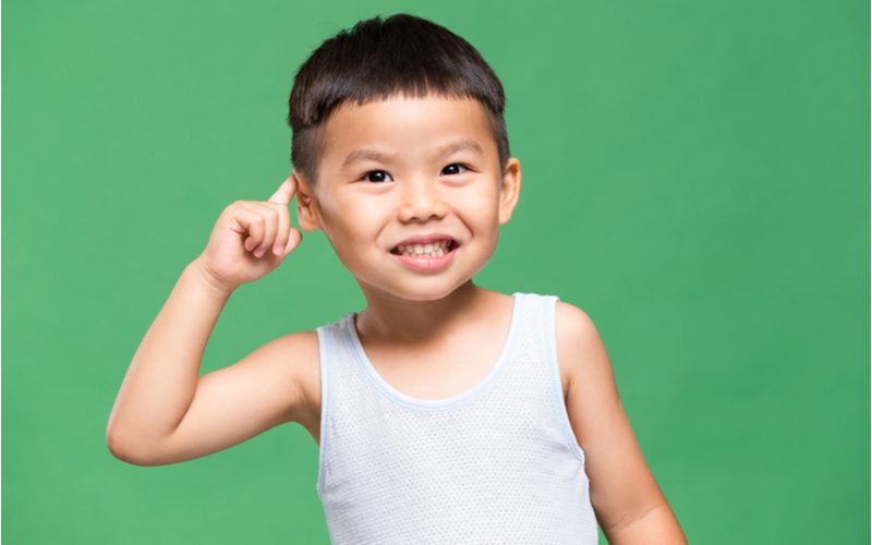 Jongenskapsel op een kleine Aziatische jongen met de rechterkant van zijn hoofd in een groene kamer