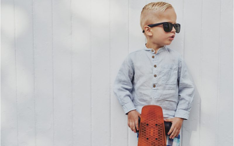 Jongetje met zonnebril en grijs button-up shirt houdt een longboard vast